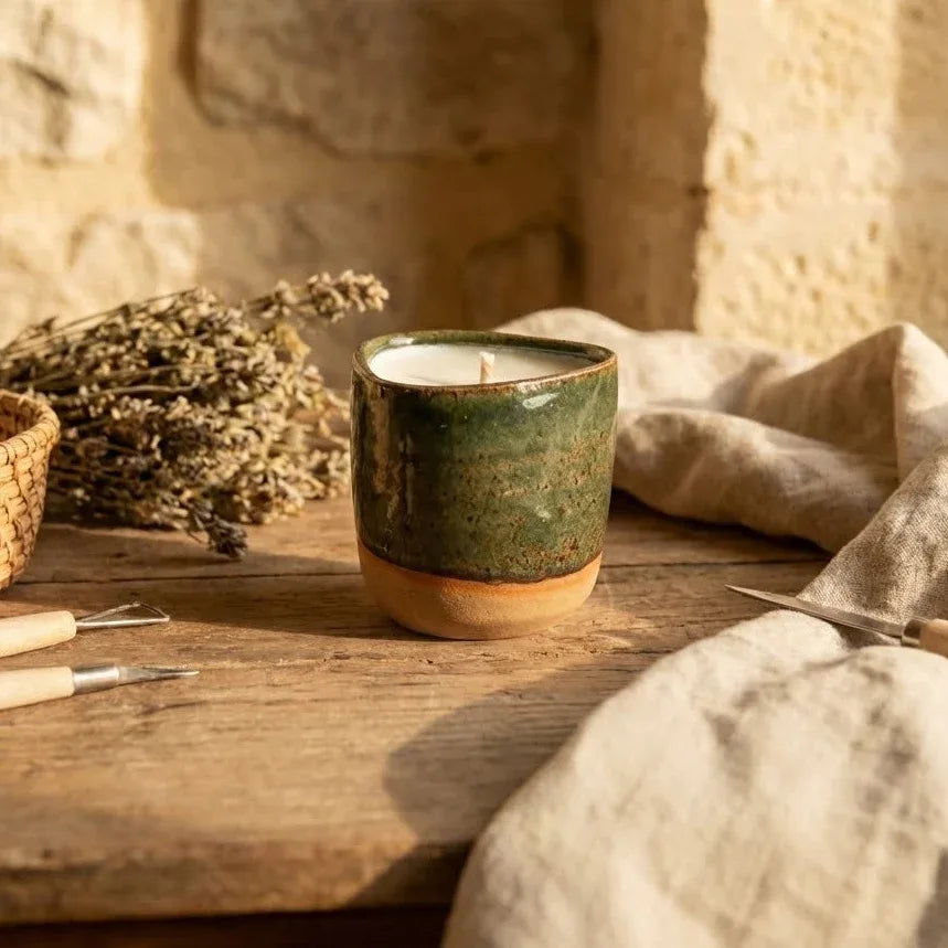 Bougie artisanale en cire végétale dans un pot en céramique rechargeable bicolore vert et terre cuite, posée sur une table en bois avec de la lavande pour une ambiance chaleureuse en Provence.