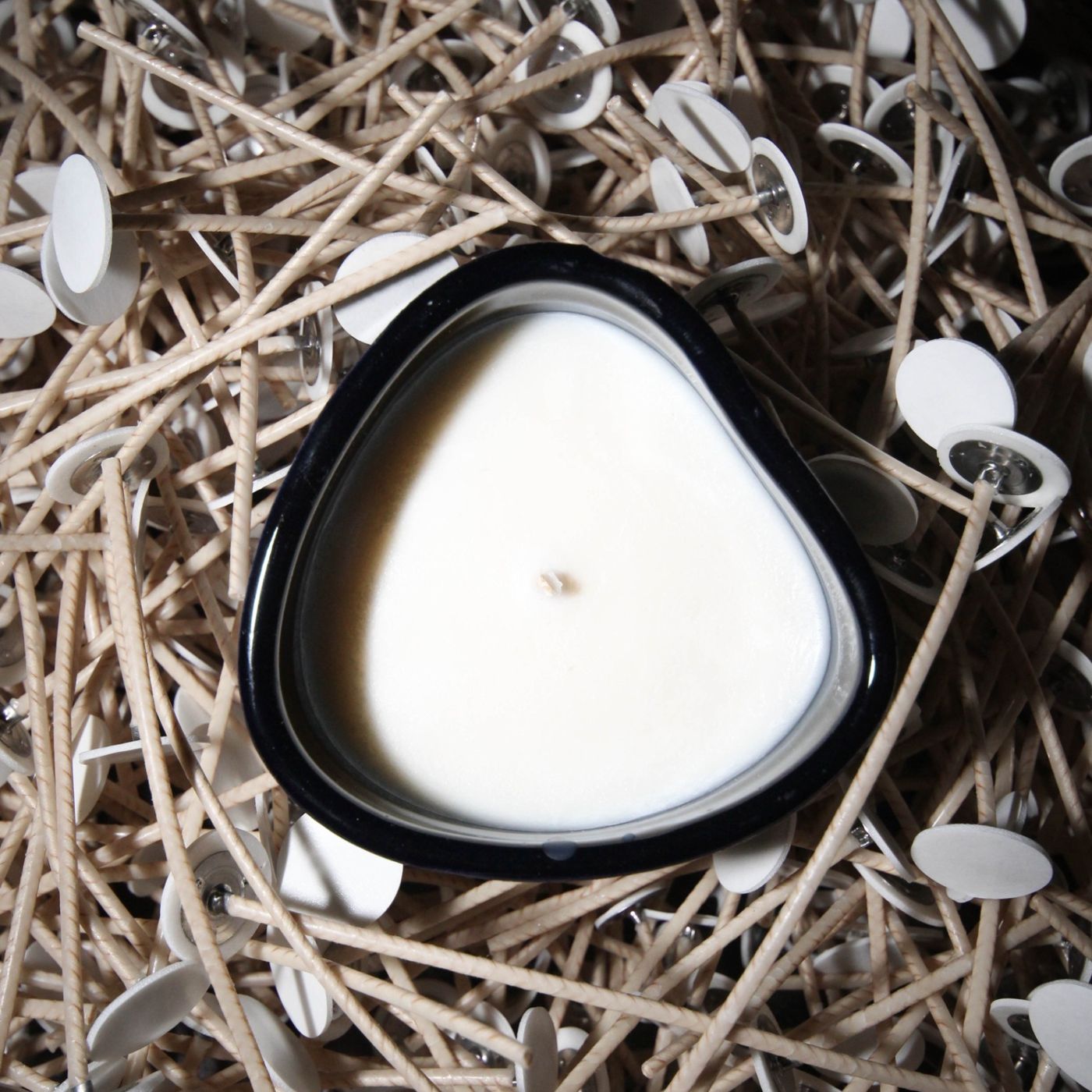 Bougie en céramique Maison Tassan avec cire végétale naturelle entourée de nombreuses mèches de bougies, illustrant la fabrication artisanale.