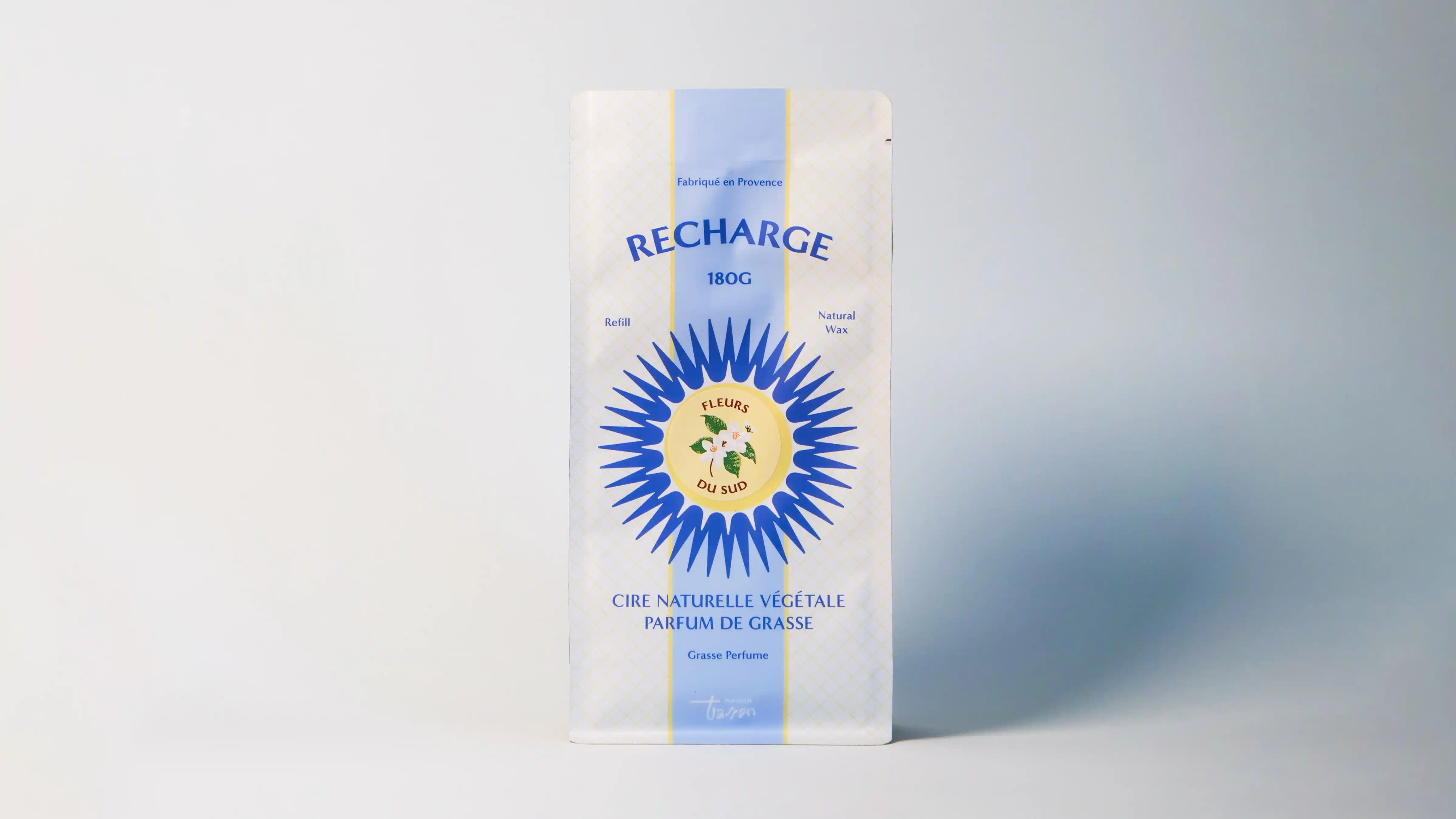 Bougie artisanale rechargeable Écorce du Ventoux allumée dans son pot en céramique vert. Mise en scène cocooning sur bois avec pommes de pin et packaging Maison Tassan. Décoration chaleureuse.