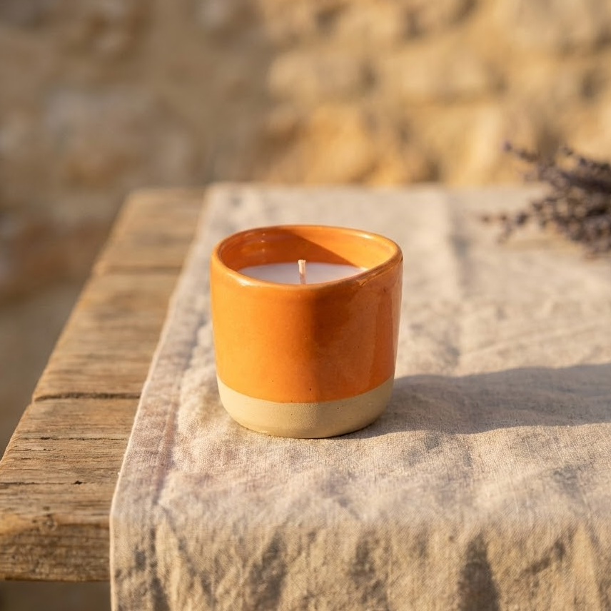 Bougie artisanale rechargeable en céramique bicolore orange et beige. Objet déco pour une ambiance chaleureuse provençale sur table en bois avec lavande séchée.